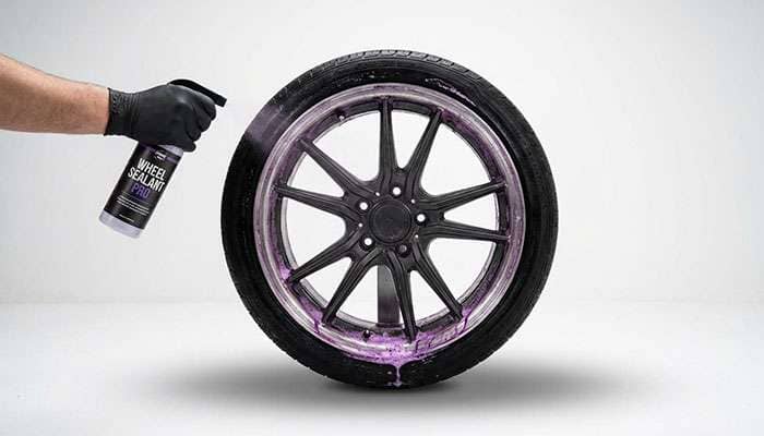 Person cleaning a car wheel with 3D Car Care spray and water, showing purple cleaner reacting on the tire rim