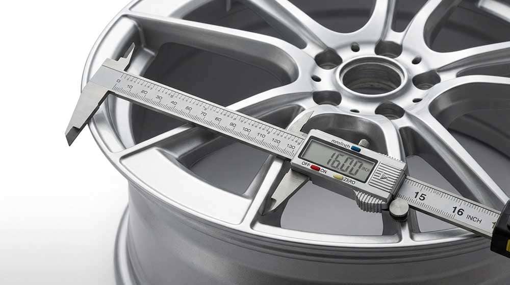 Close-up showing proper wheel width measurement for tire fitment with measuring tools