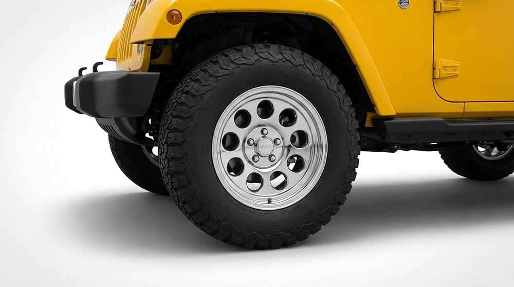 Close-up of a Jeep Wrangler tire with rugged off-road tread and polished multi-hole alloy rim on a yellow Jeep