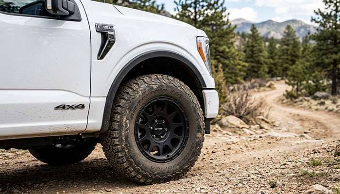 Close-up of a white Ford F-150 truck featuring rugged all-terrain tires and black alloy rims in natural light.