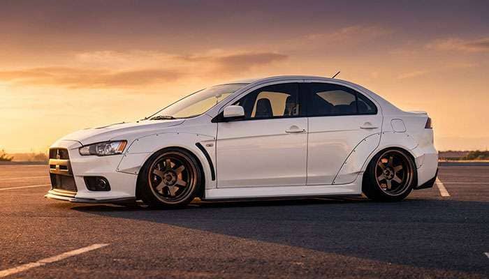 White Mitsubishi Evolution X with wide fender flares and aggressive fitment parked on asphalt at sunset.