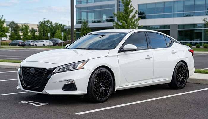 White Nissan Altima with custom black grille and aftermarket wheels parked outdoors with MODS text overlay.