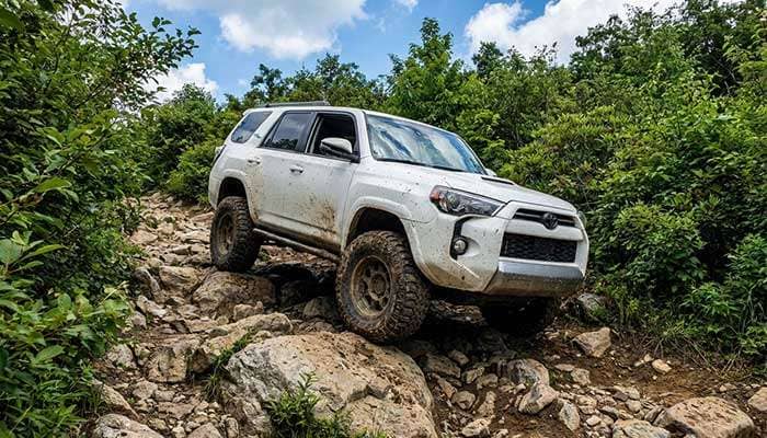 White Toyota SUV driving off-road down a rocky hill with greenery and blue sky in the background