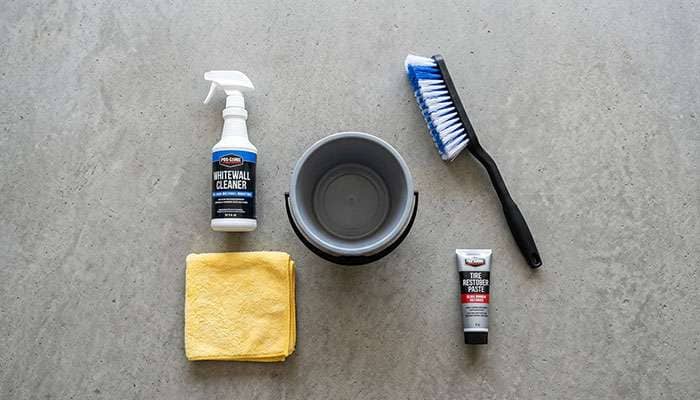 Whitewall tire cleaning supplies including brushes, tire cleaner, and microfiber towels laid out on a garage floor