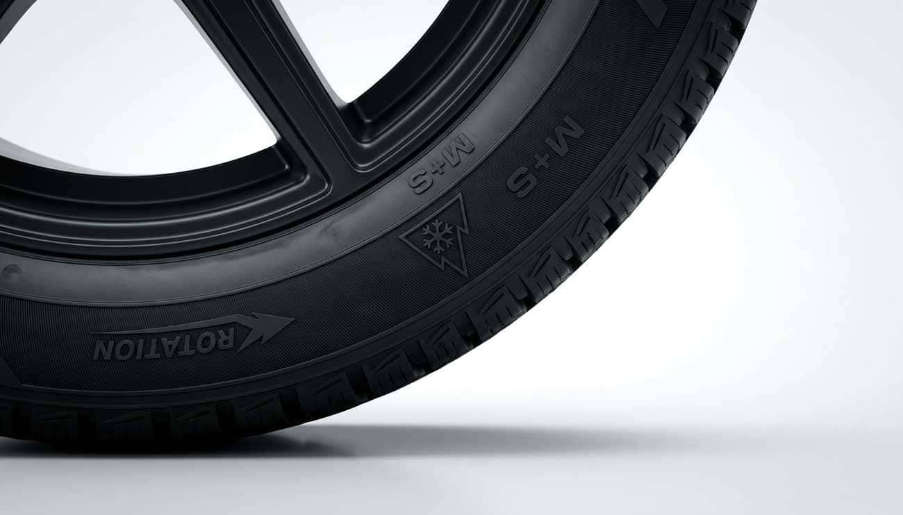 Close-up side view of a new winter tire showing the rotation arrow, snowflake symbol, and M+S marking
