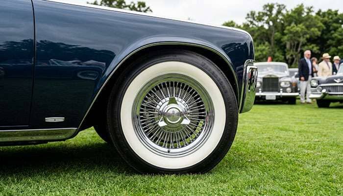 Chrome wire wheels with knock-off spinners mounted on a classic luxury car at a car show