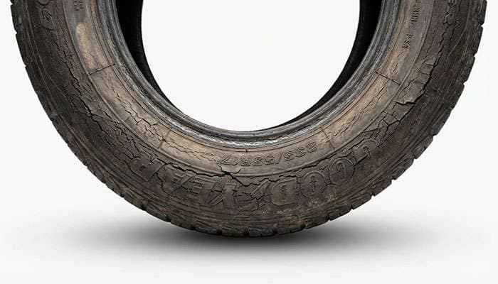Close-up of a worn and cracked tire sidewall with a visible tear and dirt marks.
