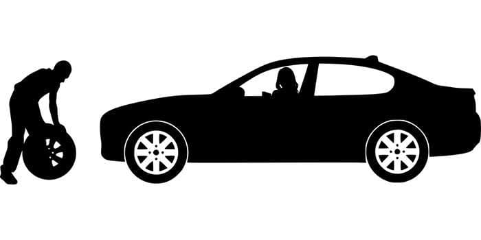 Silhouette of a car mechanic replacing a tire in an automotive repair shop with tools and equipment nearby.