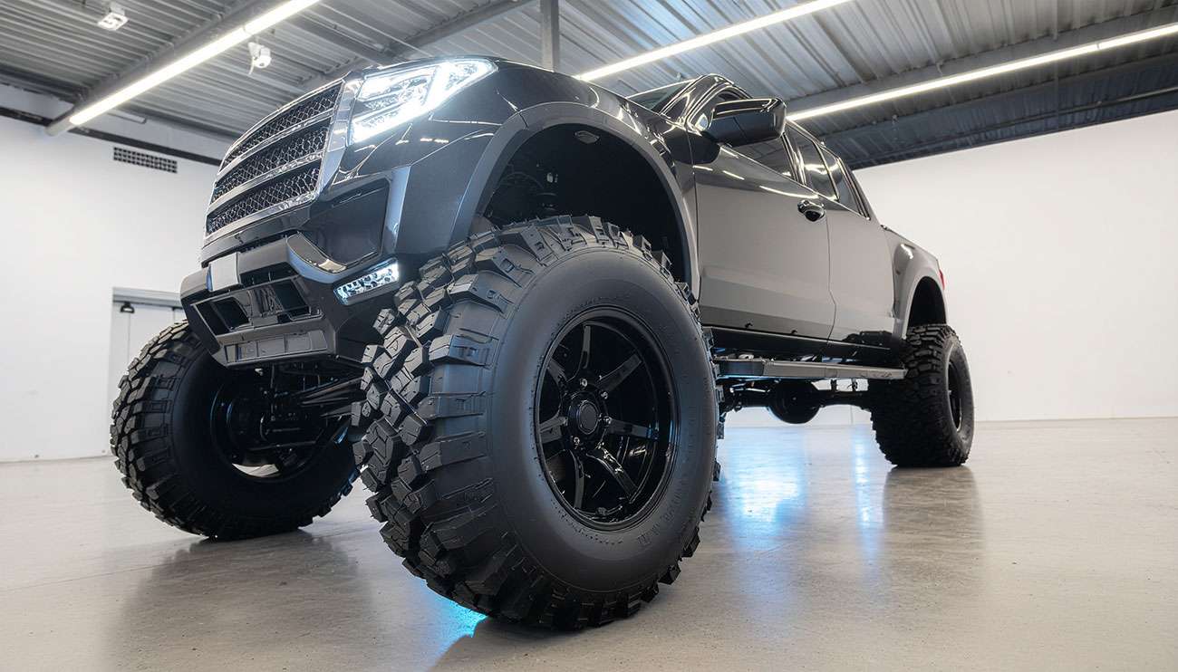 Close-up of large off-road tires mounted on a lifted black truck in a showroom setting