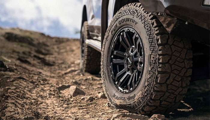 Close-up of a 4x4 off-road vehicle tire on a rocky dirt trail, highlighting rugged tread and black alloy wheel