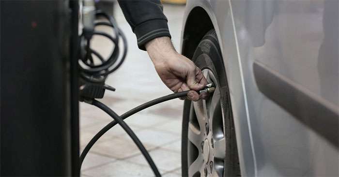 Mechanic inflating a car tire using an air hose inside an auto repair shop to ensure proper tire pressure.