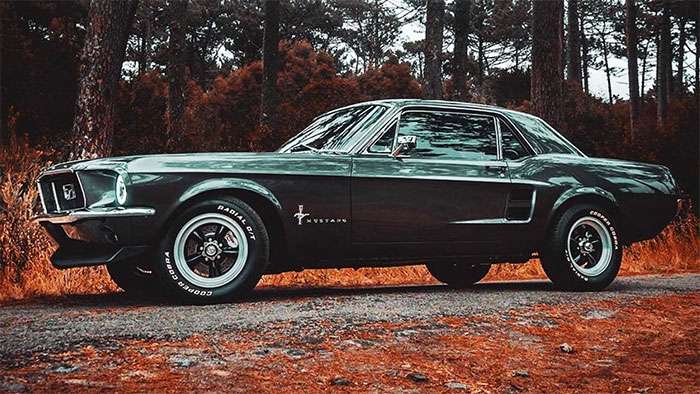 Side view of a classic dark green Ford Mustang with American Racing Vintage VN105 wheels in a forest setting.