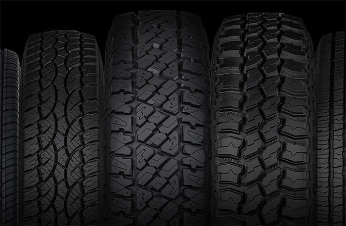 Close-up of five black vehicle tires with varied tread patterns against a black background