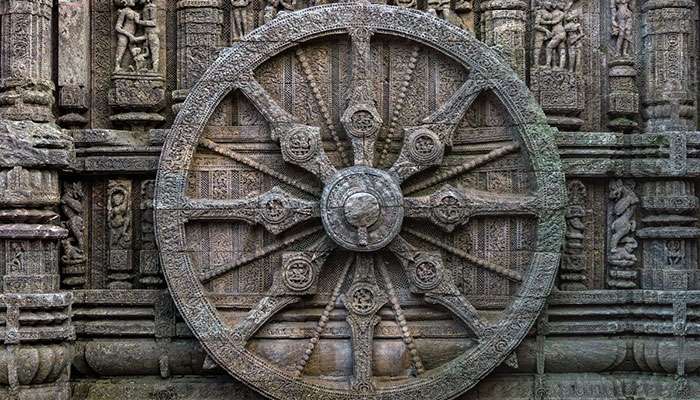 Intricately carved ancient stone wheel with detailed sculptures on surrounding temple walls, symbolizing historical significance.