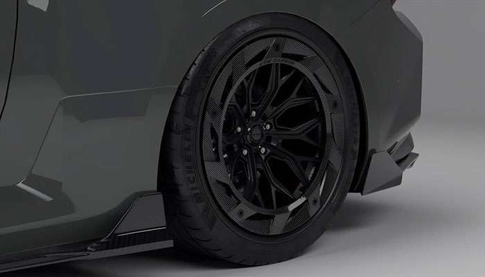 Close-up of black flow-formed carbon fiber wheel on dark gray sports car against gray background