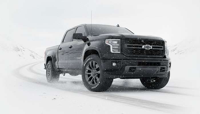 Black pickup truck driving on snowy road with three all-season truck tires displayed beside it and bold text about snow tires