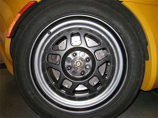 Close-up of Blackwatch Racing three-piece Bogart wheel mounted on yellow car showing visible brake components and forged construction