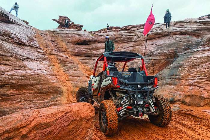 Can-Am UTV navigating rocky terrain with spectators watching from above during International Off-Road Day.