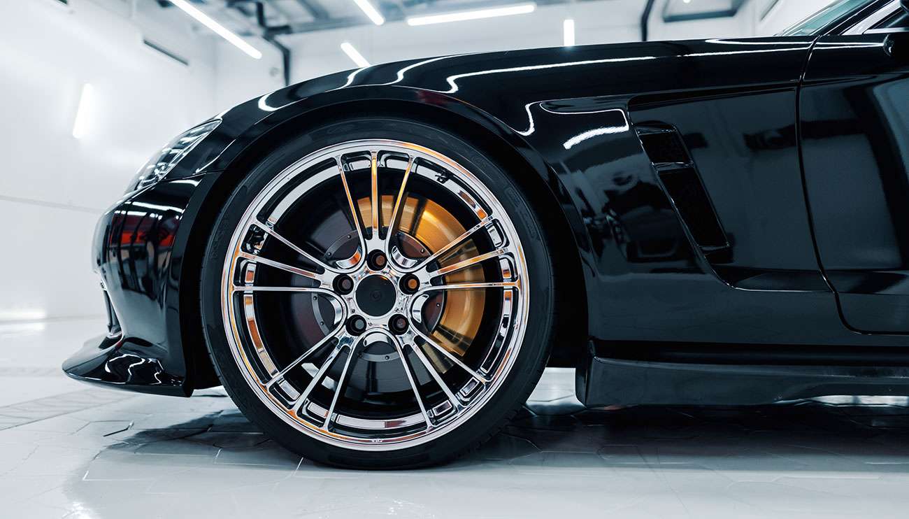 Close-up of a shiny chrome car rim on a sleek black sports car in a bright garage