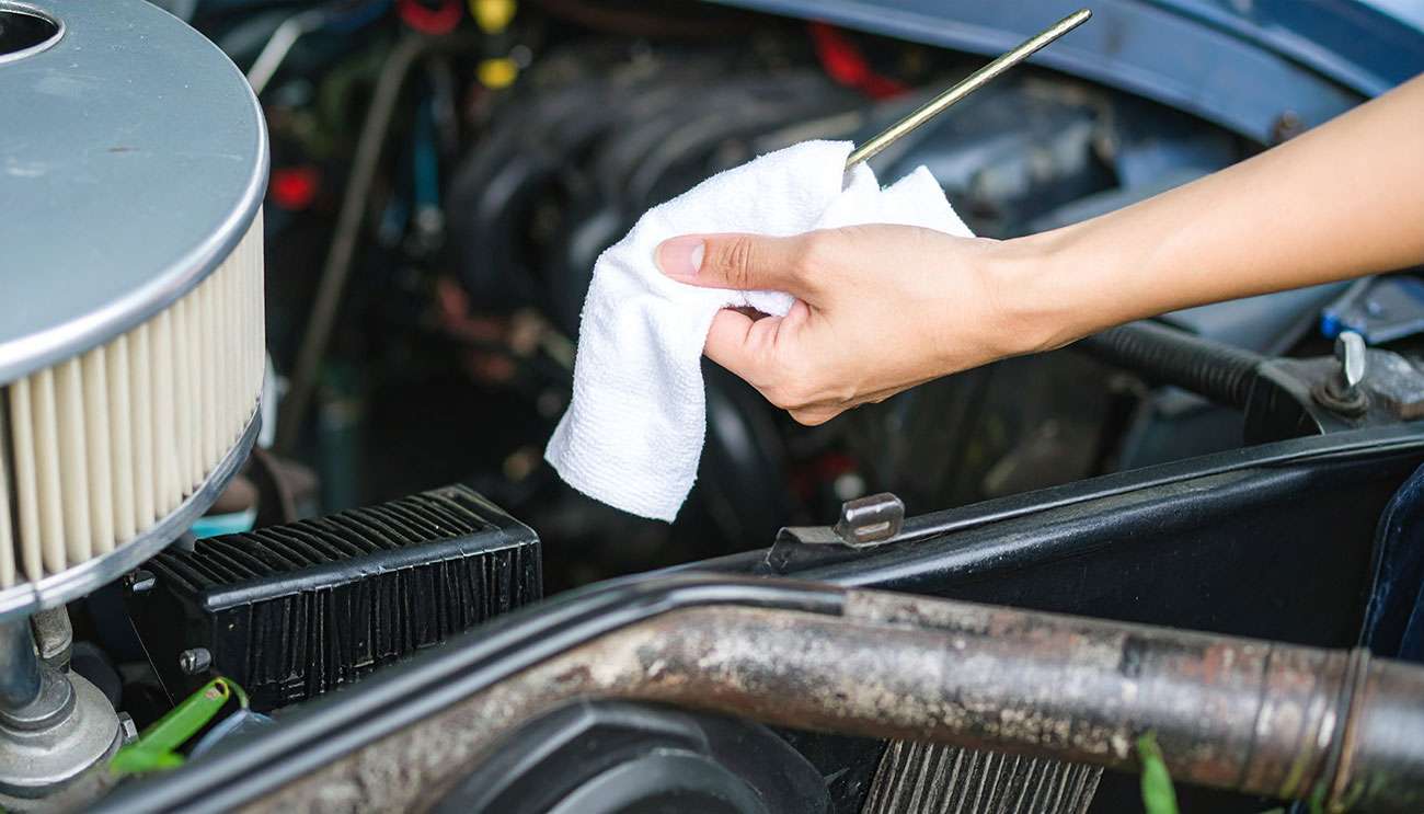 Hand cleaning a dipstick with a cloth under the hood of a classic car for maintenance.