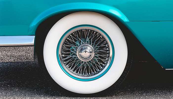 Close-up of a classic car's whitewall tire and chrome hubcap on a polished teal vintage vehicle