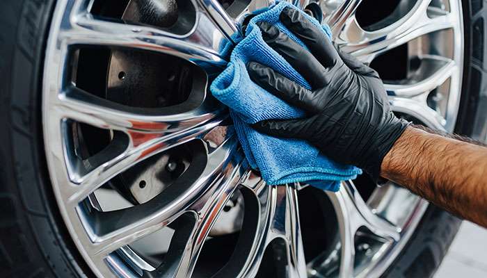 Hand cleaning a silver car wheel rim with a cloth to fix curb rash damage