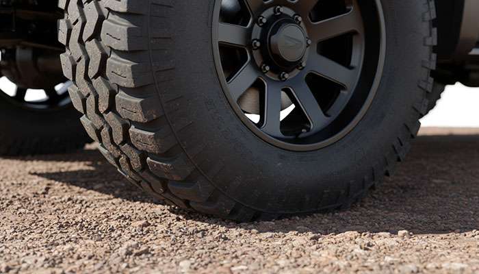 Close-up of a truck's large wheel and off-road tire on rugged outdoor terrain