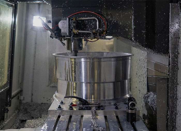 CNC machine forging a large polished metal American Force wheel rim in a factory setting with metal shavings around