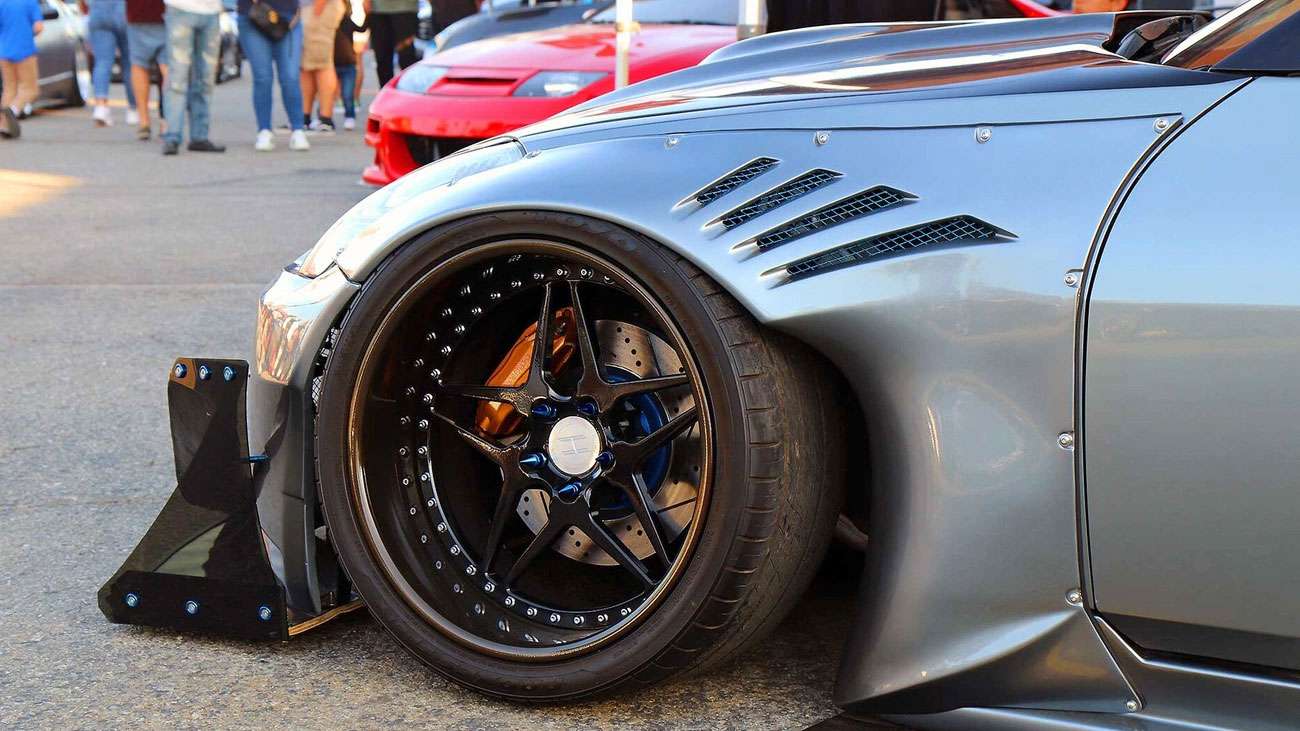 Close-up of a custom black wheel with a low offset on a modified silver sports car at a car meet.