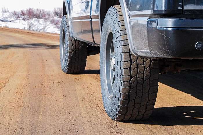 Close-up of Cooper Tires Discoverer AT3 on a truck driving on a dirt road with snow in the background