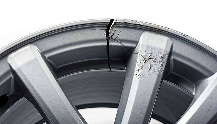 Close-up of a severely cracked silver car rim requiring repair in NYC