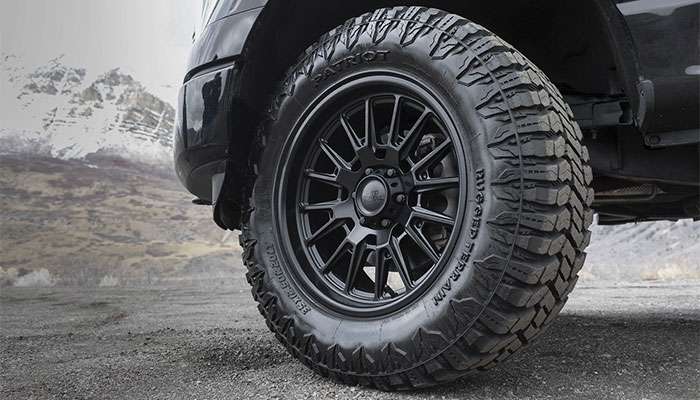 Close-up of a 2023 Ford F150 with black Moto Metal TEKTON off-road wheels and rugged Patriot tires on a gravel road