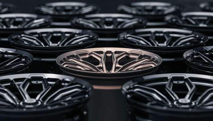 Close-up of multiple forged alloy wheels with one bronze-colored wheel highlighted among black wheels in factory setting