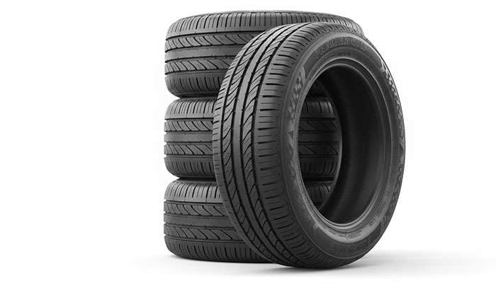 Stack of four new black car tires with detailed tread patterns on a white background