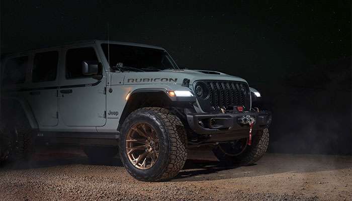 2023 gray Jeep Wrangler Rubicon with Fuel FLAME off-road wheels parked on dirt at night with headlights on.