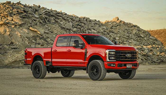 Red Ford Super Duty truck with Fuel Wheels parked on grass under trees displaying aftermarket wheel performance