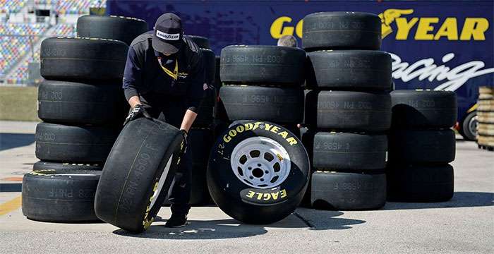 Goodyear team member handling racing tires stacked near a Goodyear Racing sign at a racetrack pit area