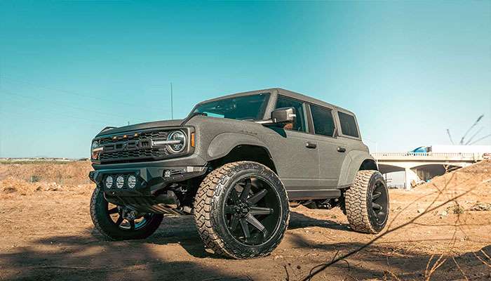 Close-up of a black Raptor truck's rear wheel kicking up dust on a dirt road in an offroad setting