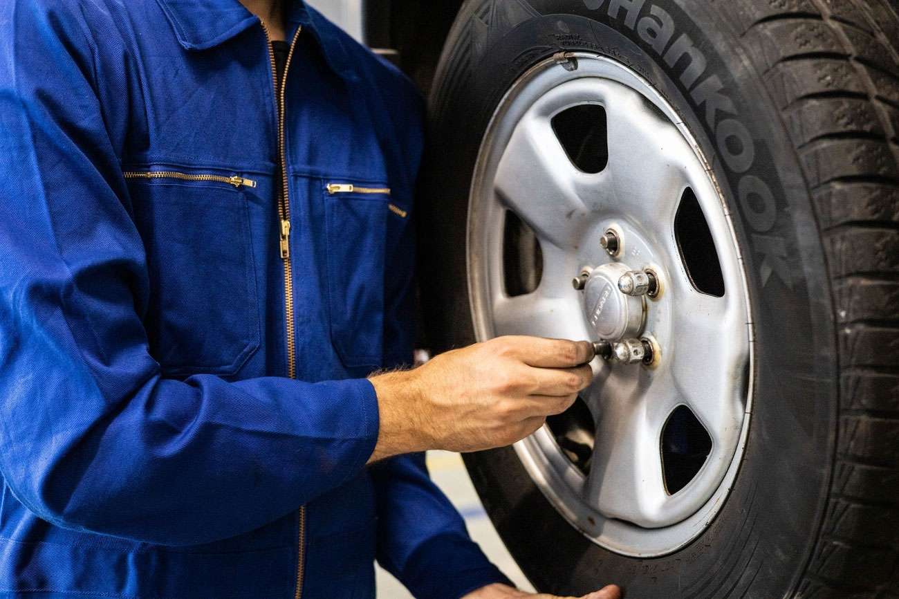 Mechanic in blue coveralls tightening lug nuts on a car tire for preventative maintenance and service.