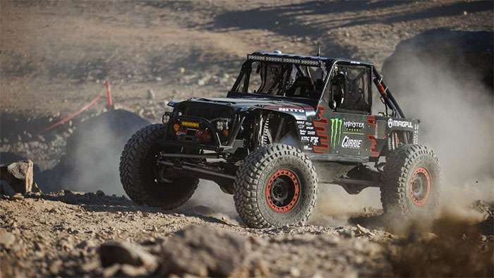 Off-road rock crawler vehicle racing in the 2022 King of the Hammers desert event kicking up dust