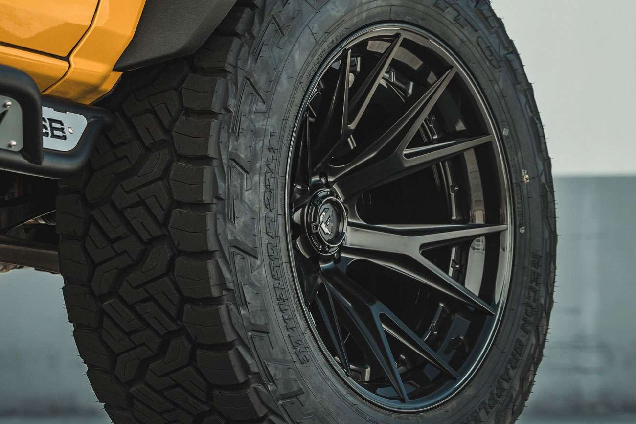 Close-up of a rugged off-road truck tire with a black multi-spoke alloy wheel on a yellow vehicle.