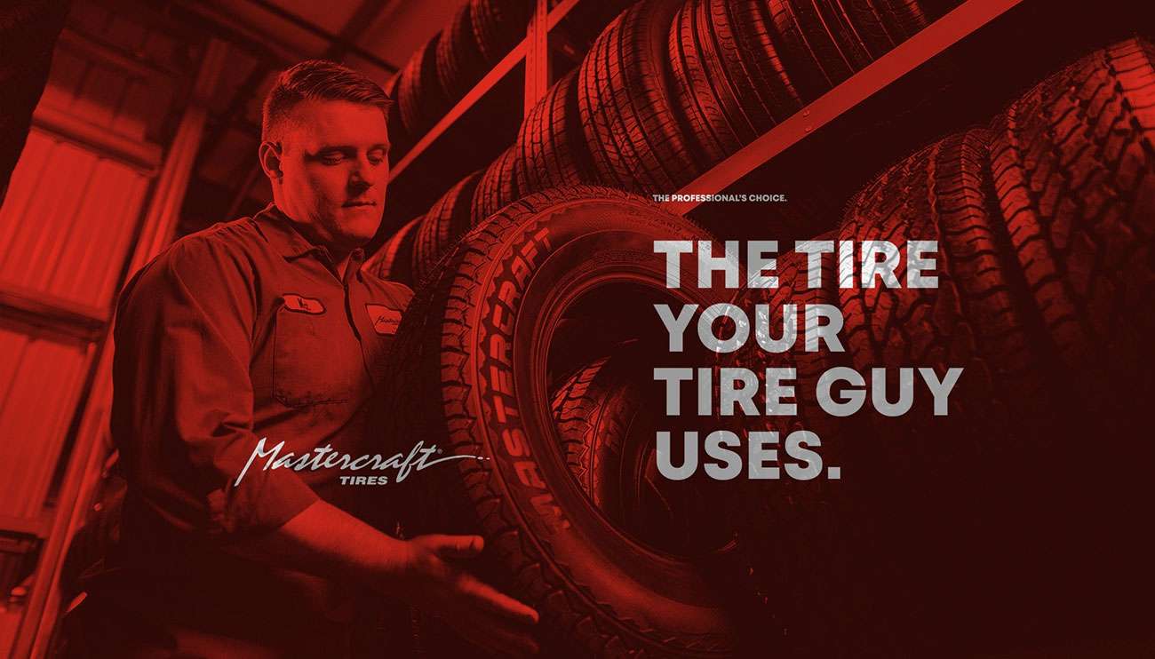 Close-up of a car's Mastercraft tire and black alloy wheel in a professional auto service garage