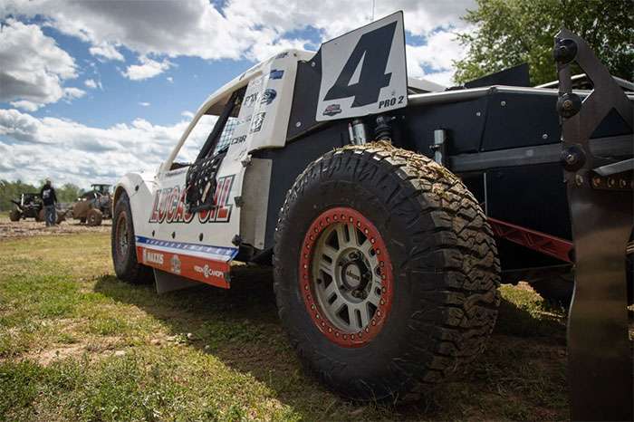 Off-road race truck number 4 with Lucas Oil and Maxxis logos parked on grass under a partly cloudy sky