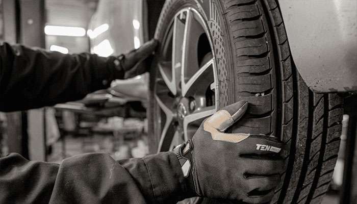Mechanic wearing gloves inspecting a car tire in a workshop, highlighting tire maintenance services.