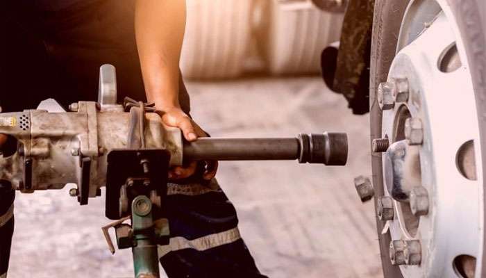 Mechanic using a power tool to install or inspect lug nuts on a large vehicle's wheel