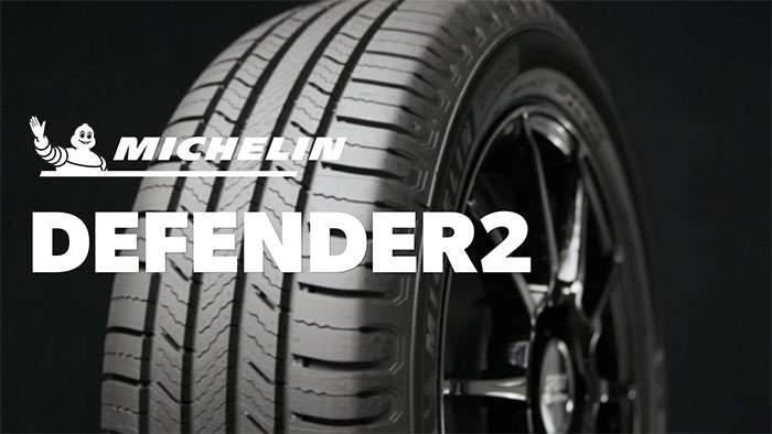 Close-up of a Michelin Defender2 tire showcasing tread design and black alloy wheel on a dark background