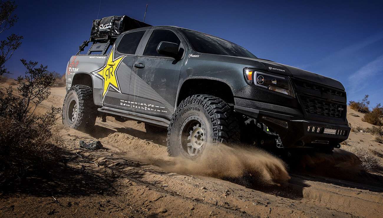 Close-up of a rugged off-road tire on a vehicle driving over red desert terrain at sunset