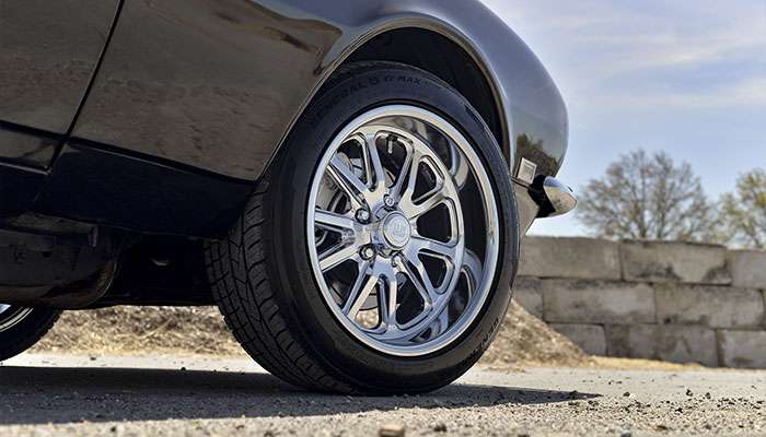 Close-up of a black muscle car's alloy wheel on a paved road