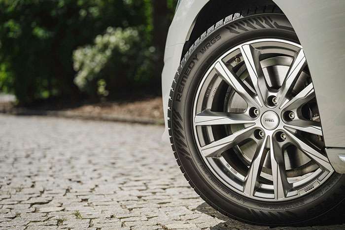 Close-up of a Nokian Tires Remedy WRG5 tire on a car parked on a cobblestone road, promoting fuel economy