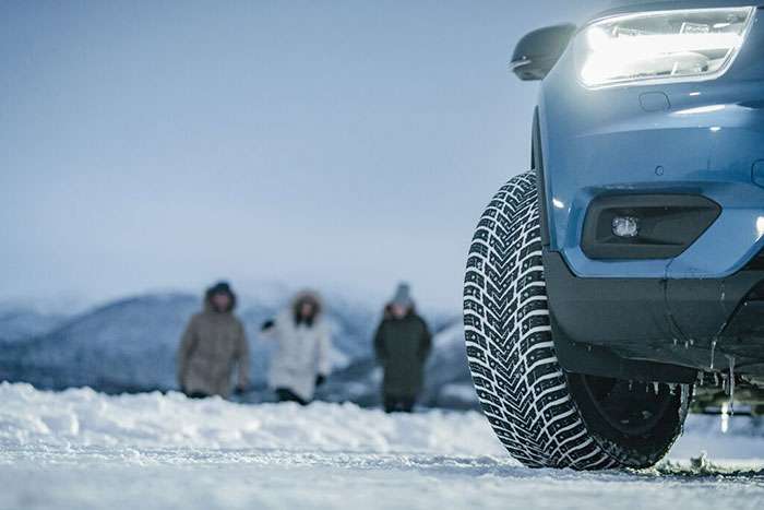 Close-up of a Nokian Tires winter tire on a snow-covered road with pine trees in the background under a clear sky